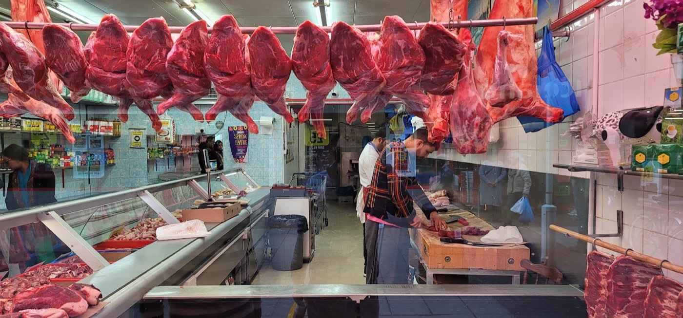 A busy butcher's stall with hanging meat at Chrisp Street Market, Poplar
