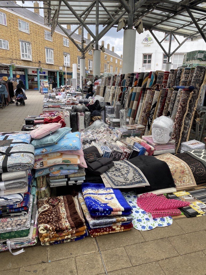 The pedestrian precinct at Chrisp Street Market with stalls, the Lansbury Estate flats and the market clock building behind